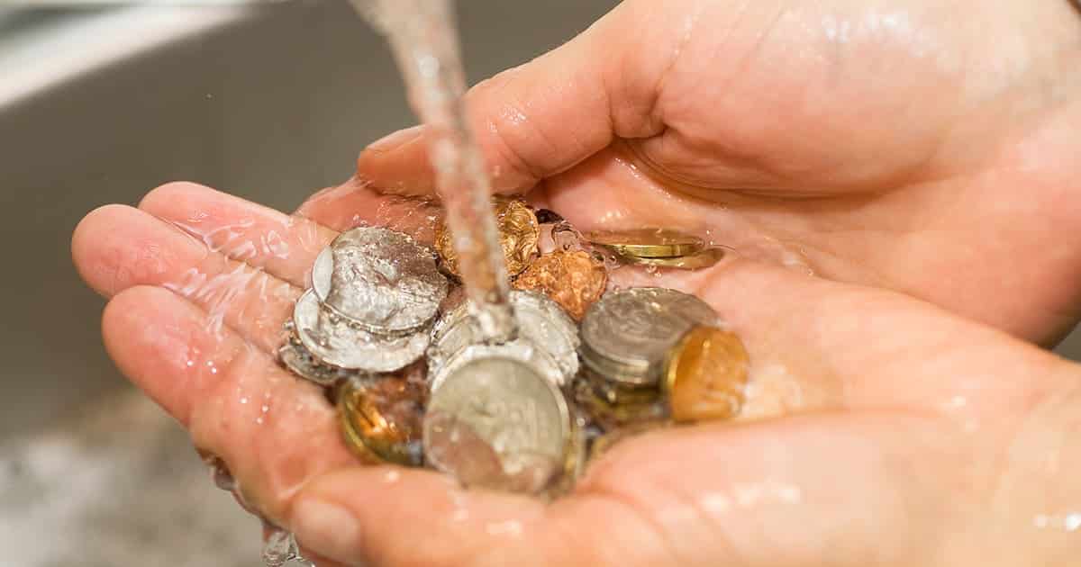 Coins in hands, under a water faucet.