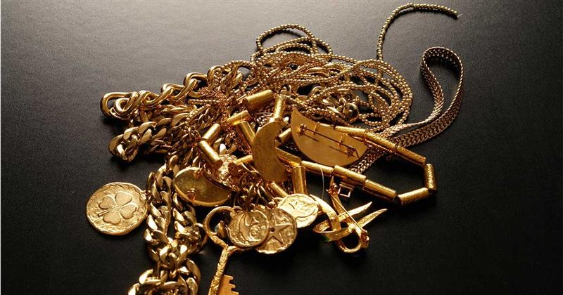 A pile of gold jewelry, coins, and charms on a black background.
