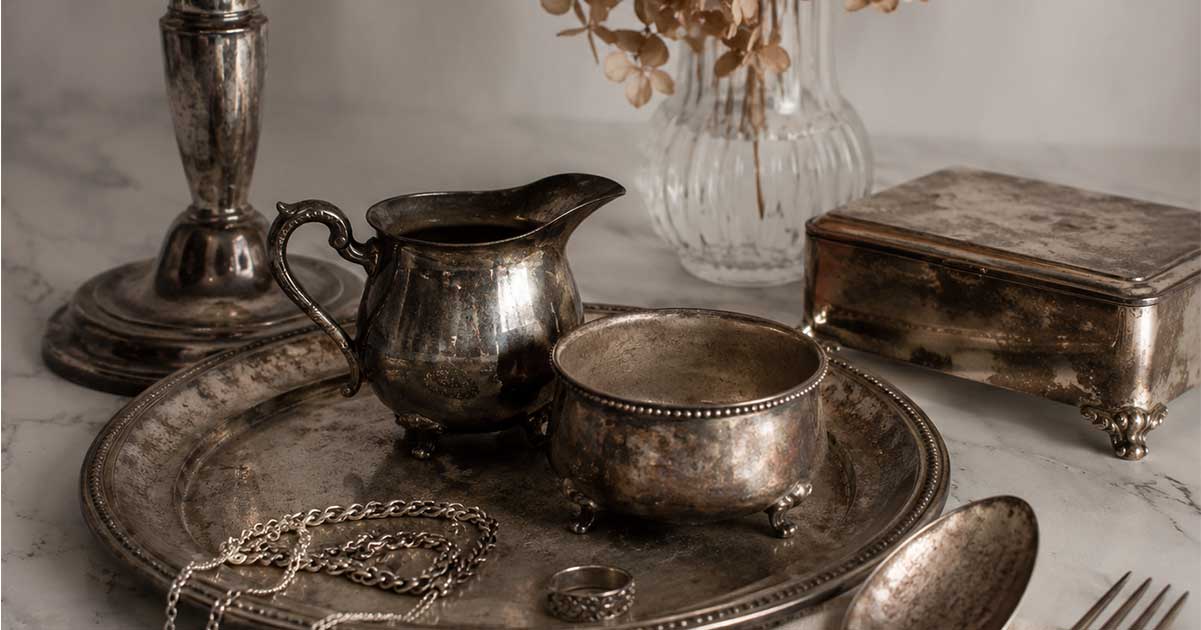 Several heavily tarnished silver items against a white background and with a flower in a vase.