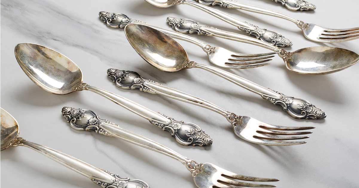 Silver spoons and sporks arranged against a white tablecloth.