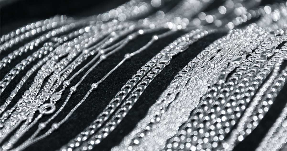 Several silver necklace chains of varying weights and styles against a black velvet background.