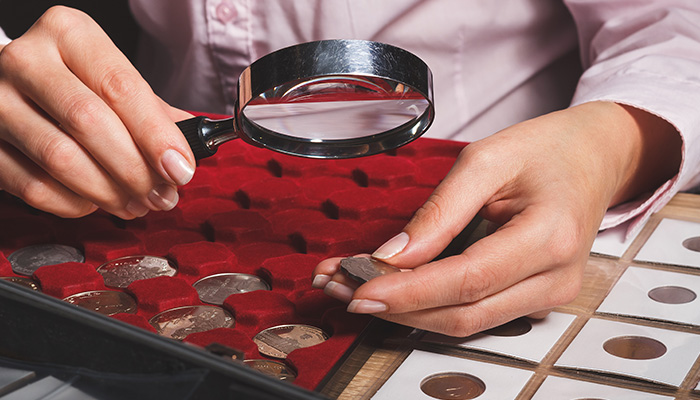 A man with a magnifying glass inspecting numismatic coins.